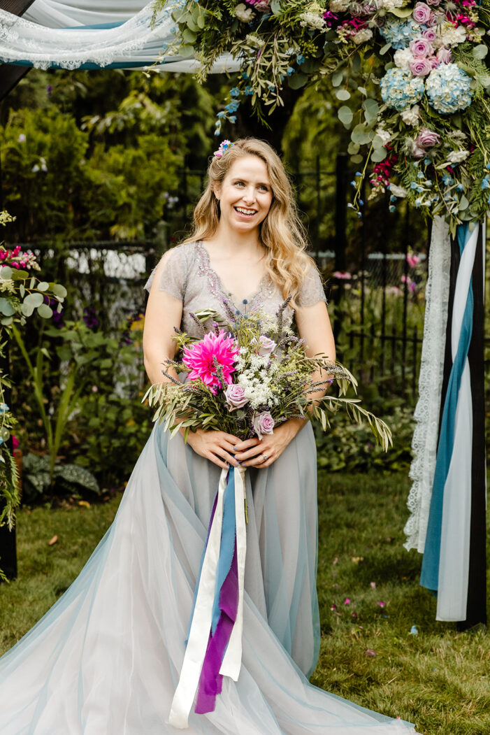 bride smiles while holding a pink and purple bouquet