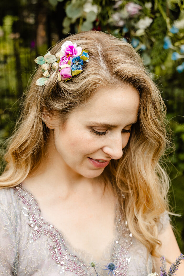 bride looks down at her bouquet with pink and blue flowers in her blond hair