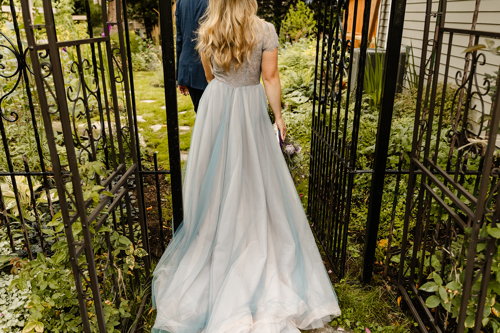 trail of blue and white wedding dress as bride walks through garden
