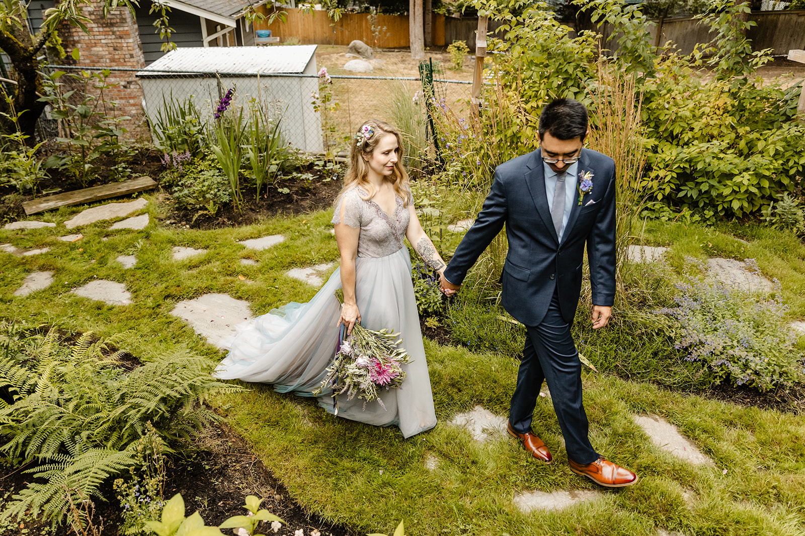 bride and groom walk through garden holding hands