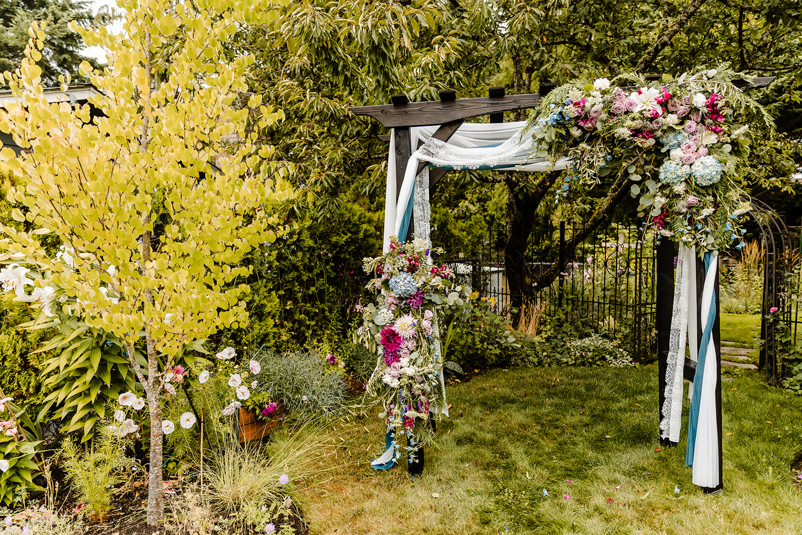 ceremony arch with purple, blue and white flowers and blue drapery