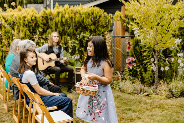 little girl in blue dress walks down ceremony aisle in backyard wedding