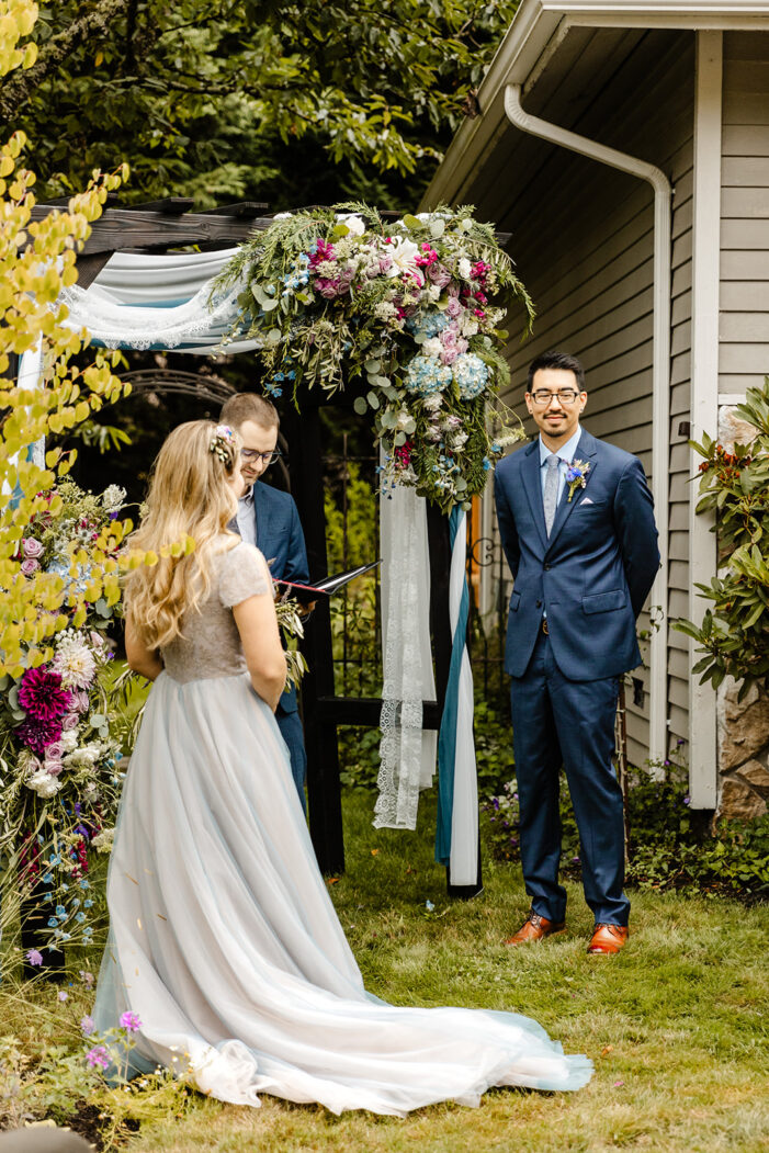 groom looks out at guests during ceremony in backyard