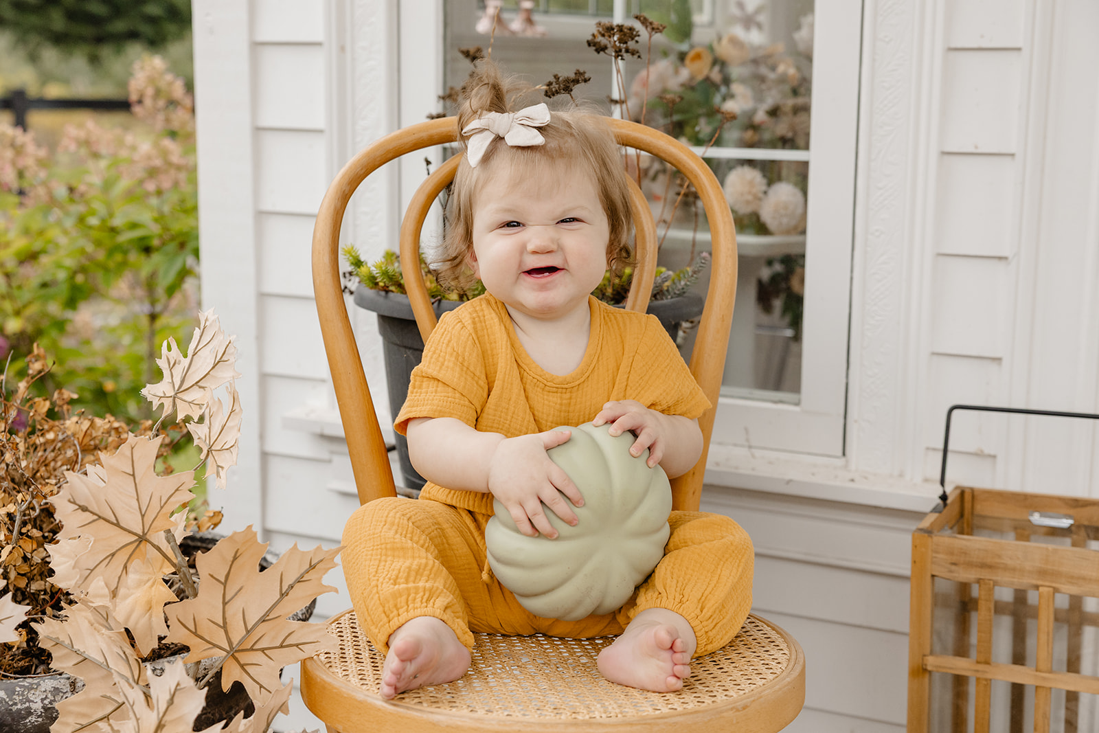 little girl holding pumpkin sitting on a chair smiling at the camera, fall family photographer near seattle washington