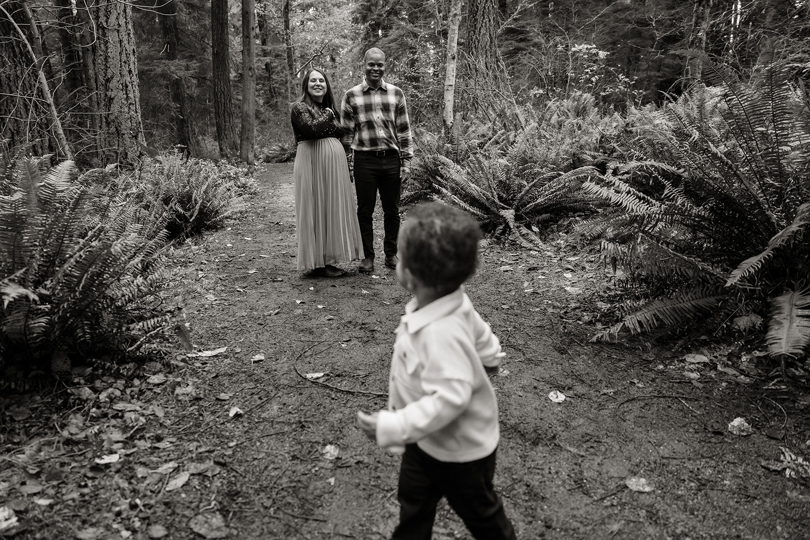 family photos in the forest in tacoma washington, seattle family photographer, son running away from parents looking back smiling