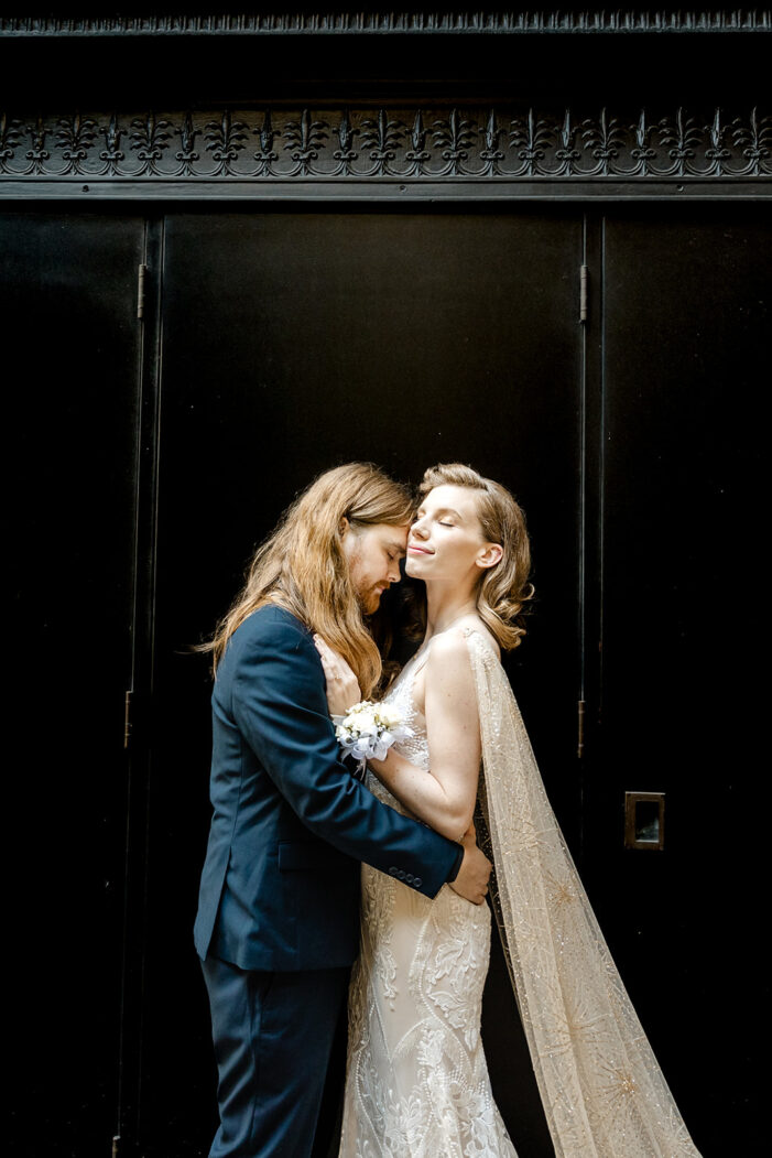 bride and groom snuggle in front of a black wall