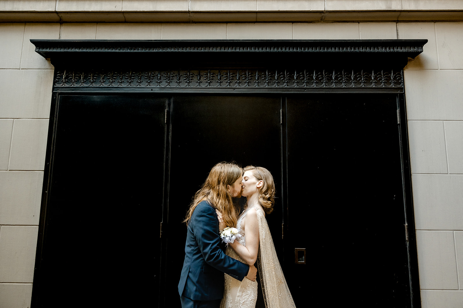 bride and groom snuggle in front of black wall
