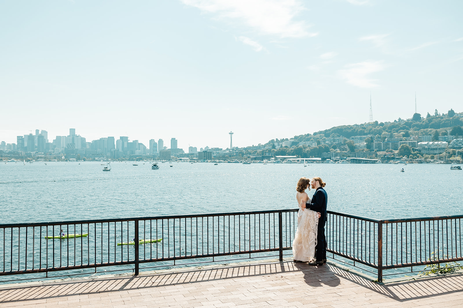 bride and groom pose against fence with seattle skyline in back