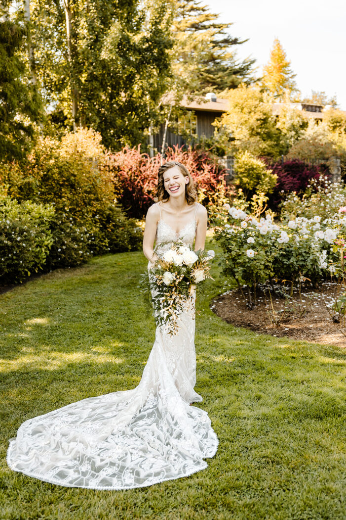 bride laughs in rose garden while holding white and green bouquet