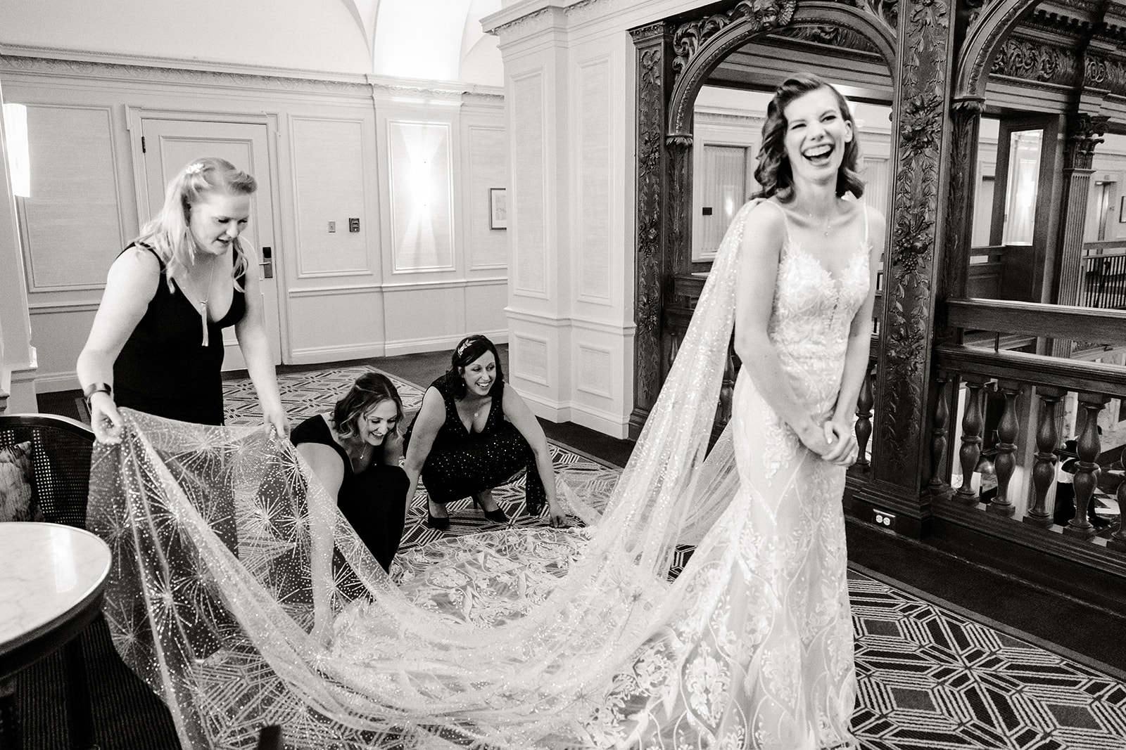bride stands in hallway with bridesmaids holding train