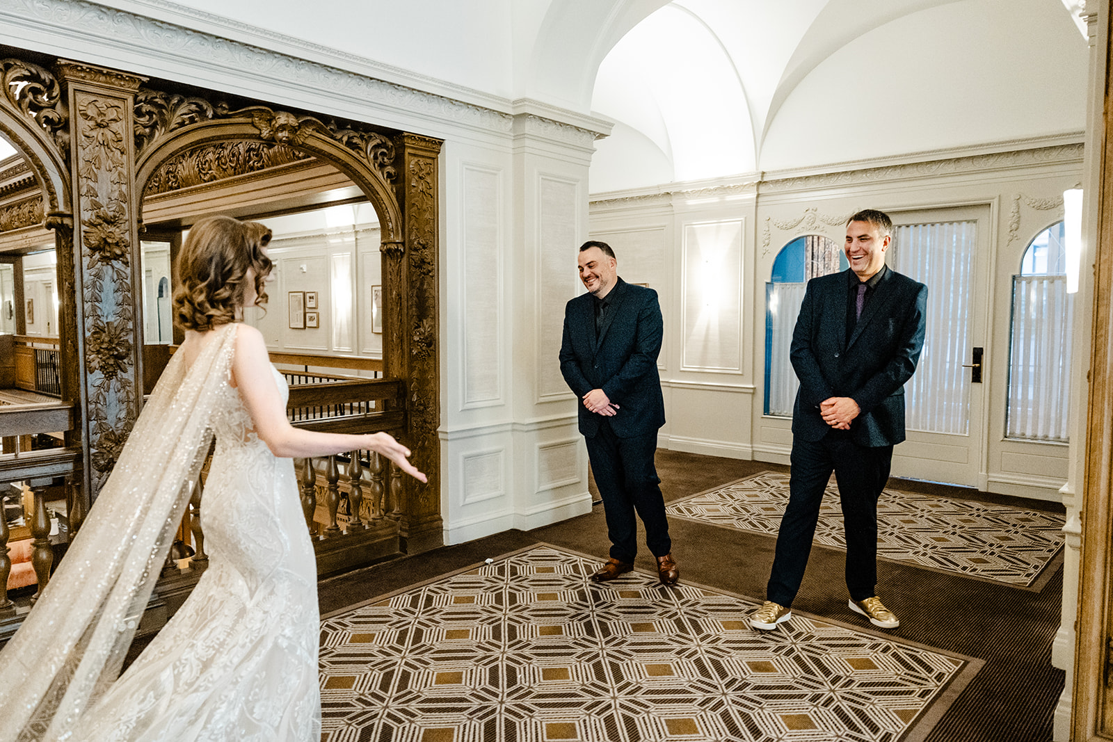 bride stands in front of two men showing off dress