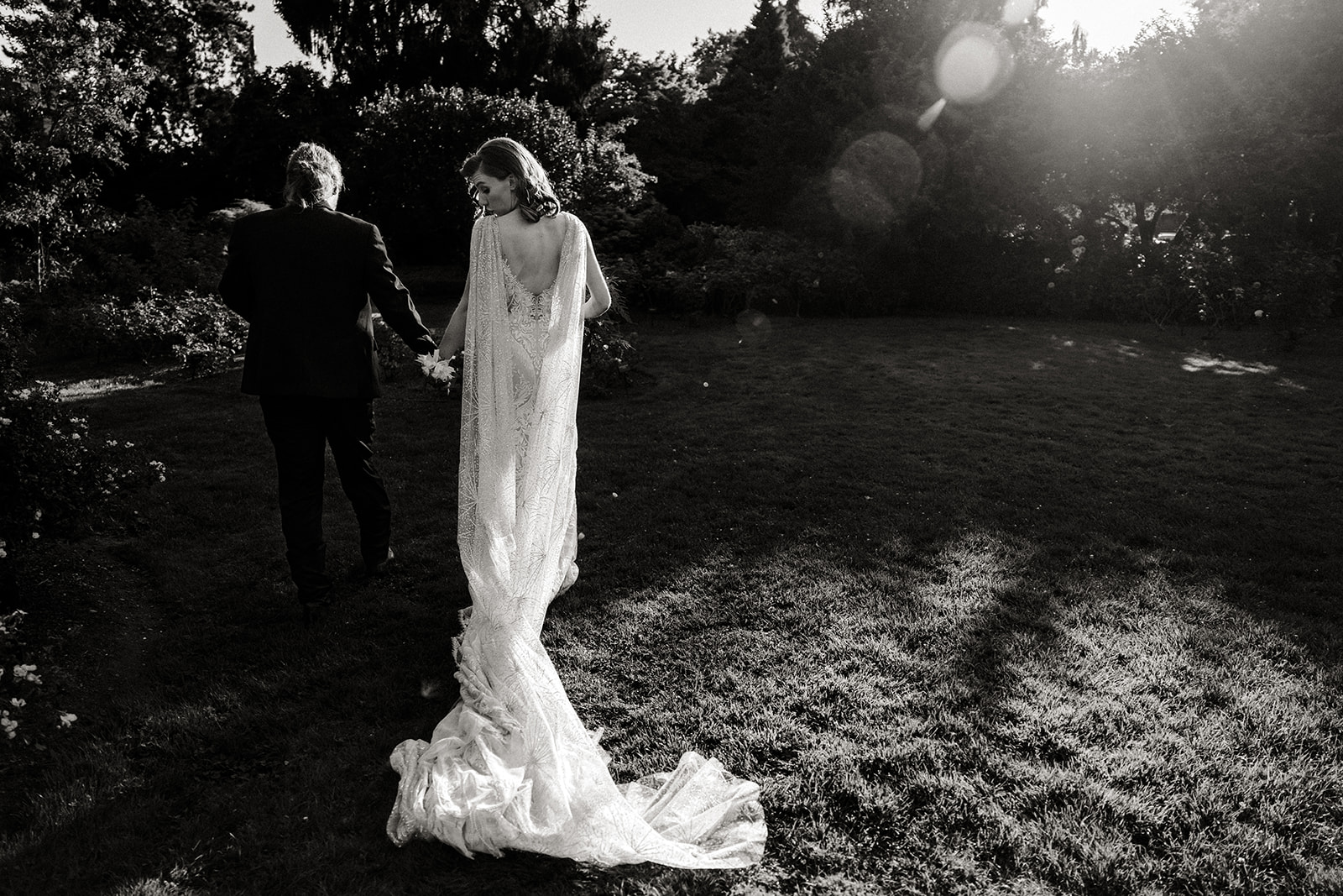 bride and groom walk across a field with her dress trailing behind her