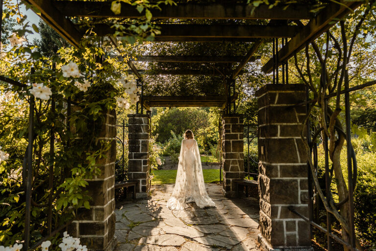 bride stands under trellis covered in roses