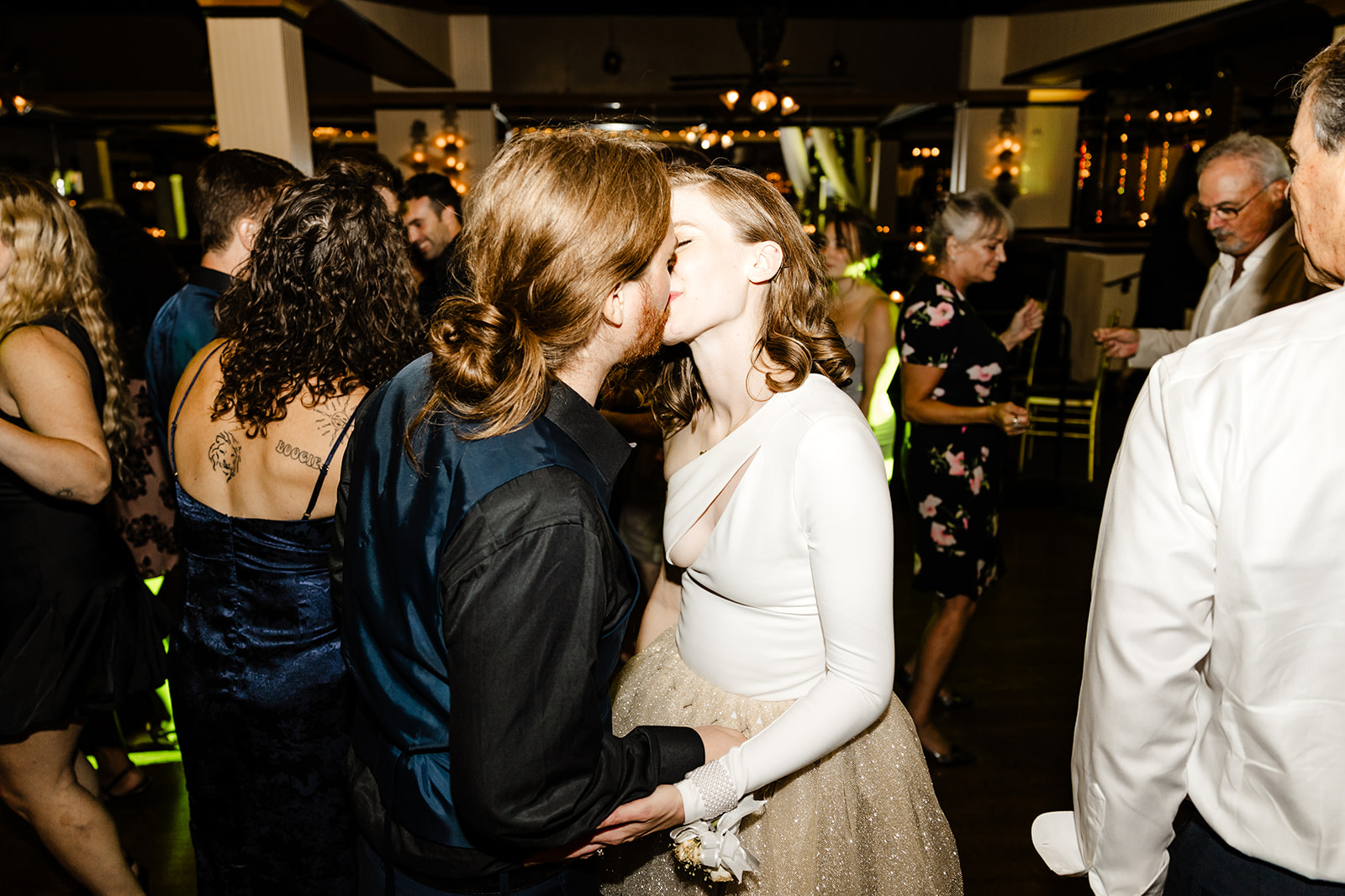 bride and groom kiss on dance floor while surrounded by wedding guests