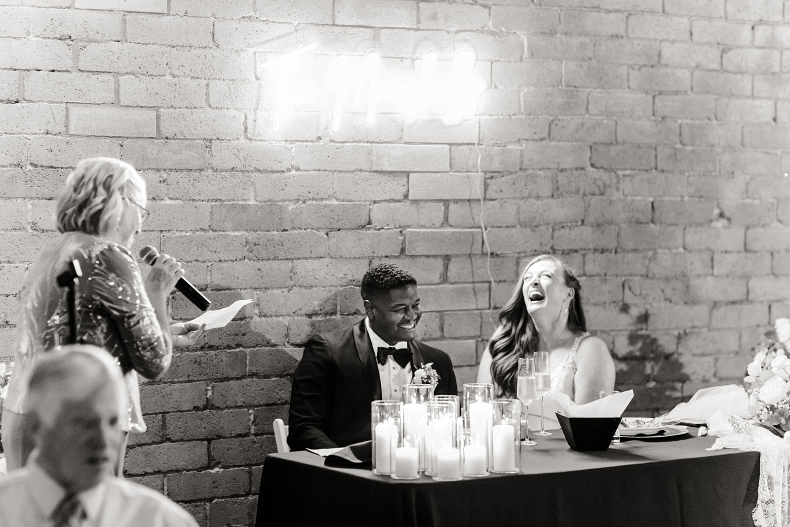 bride and groom laugh at someone giving a speech