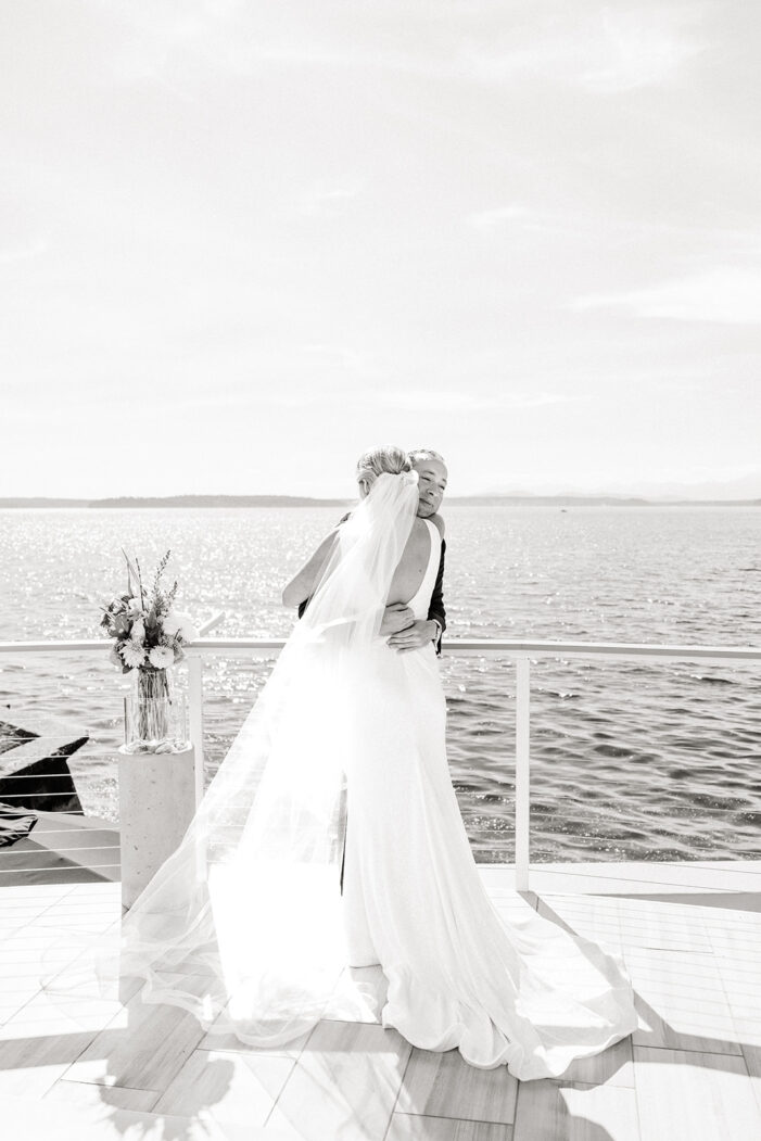bride and groom hug on porch overlooking ocean
