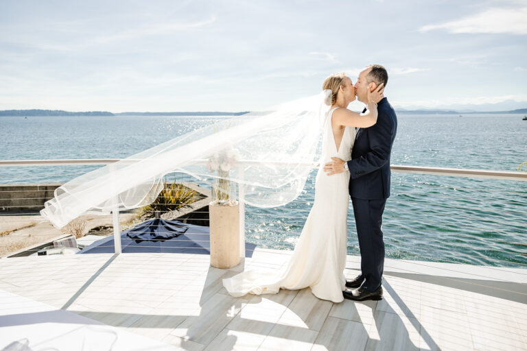 bride and groom kiss while veil trails behind her