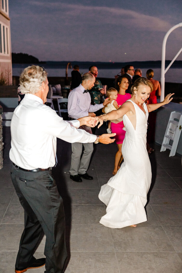 wedding guests dance with ocean and sunset behind them