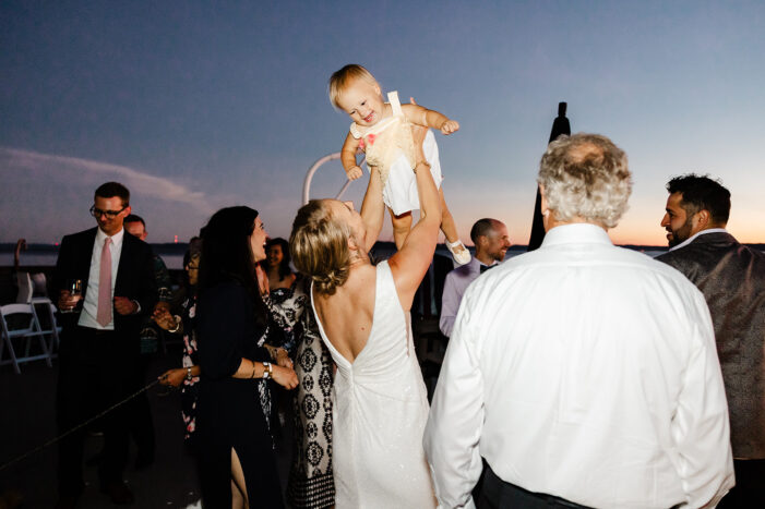 wedding guests dance with ocean and sunset behind them