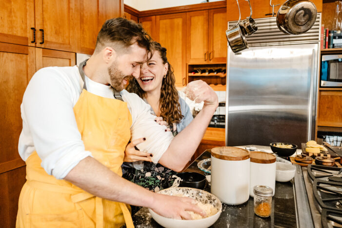 man and woman laugh together as they bake in a kitchen