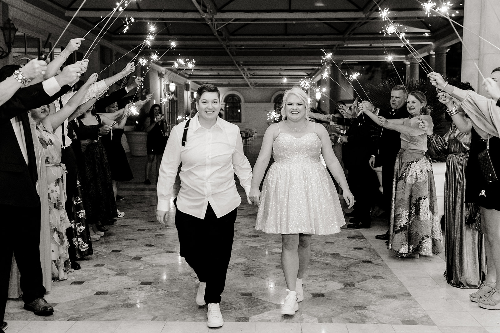 two bridges walk hand in hand through row of sparklers leaving their wedding
