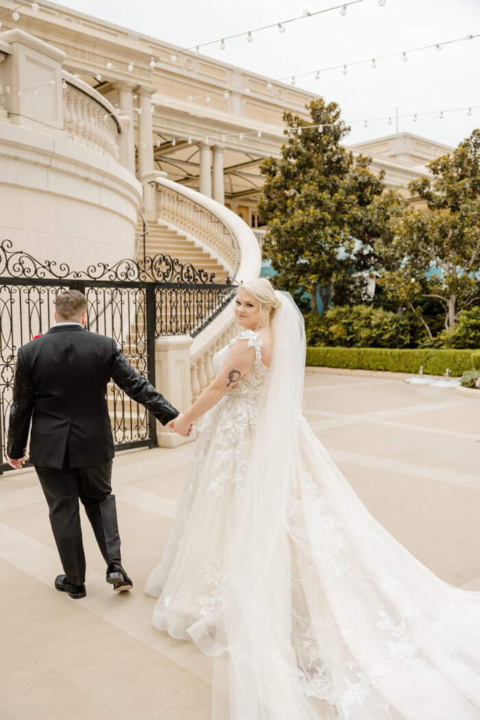 two brides walk towards iron gate, one of the brides looks back over shoulder