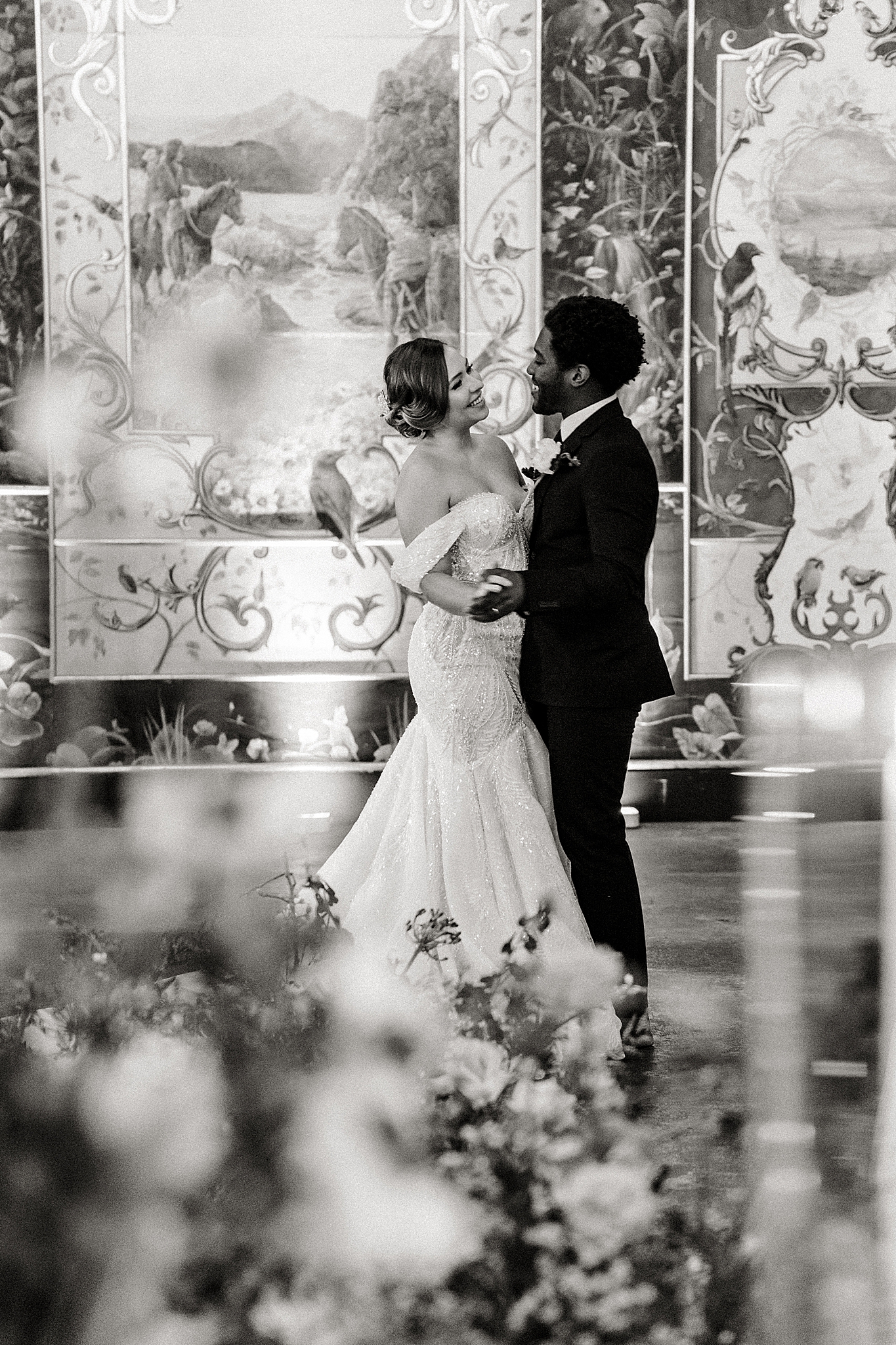 couple first dance surrounded by candlelight and flowers on reception tables, black and white photo