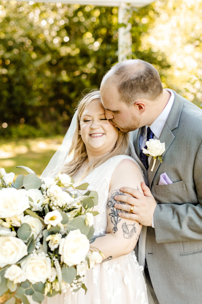 groom stands behind bride and kisses her on the cheek