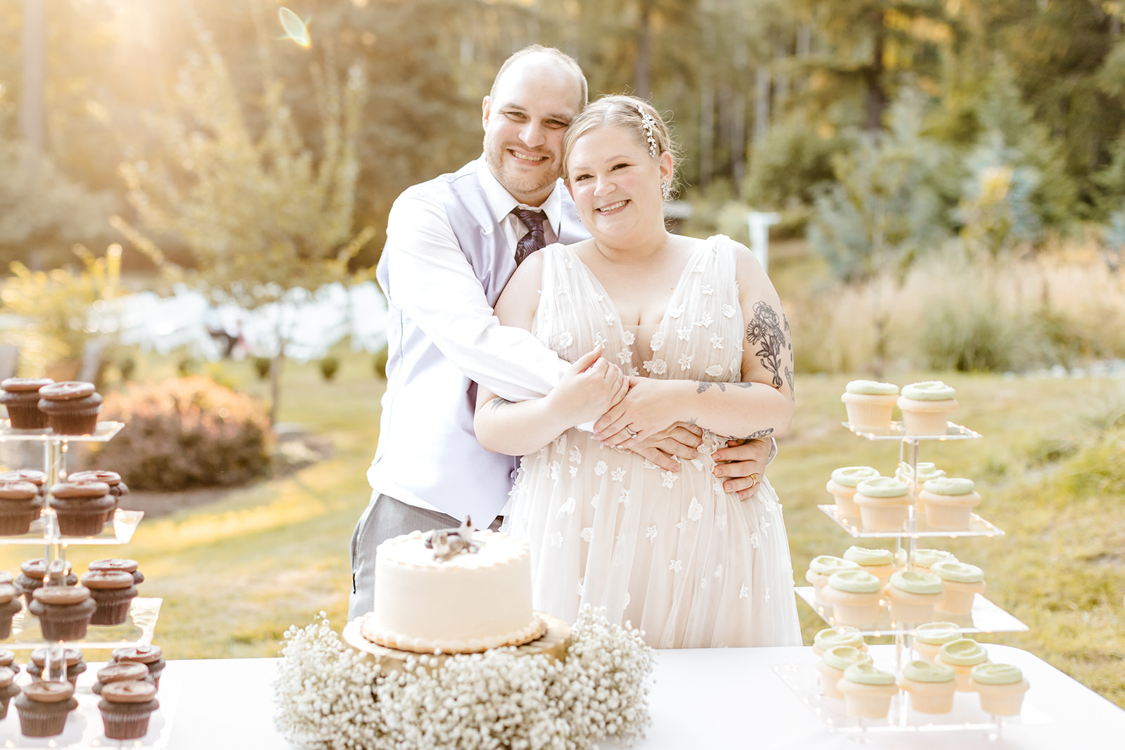 groom hugs bride from behind in front of cake table at wedding
