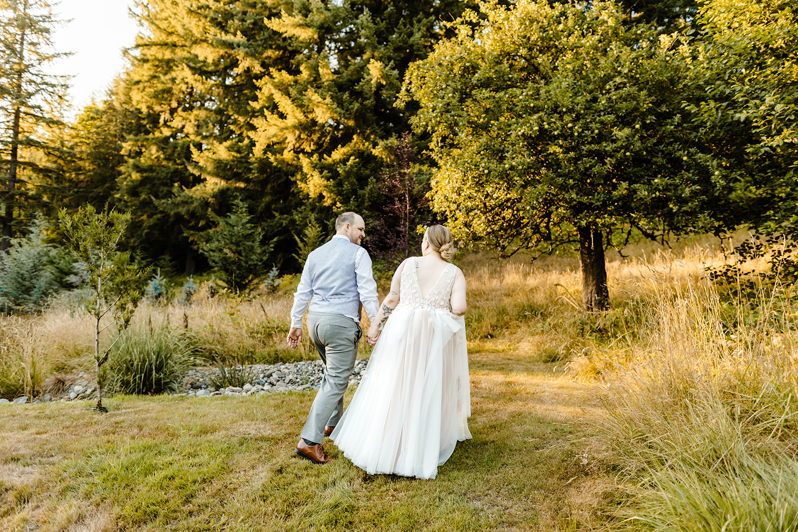bride and groom walk through field at sunset together