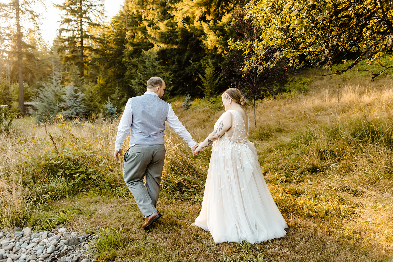 bride and groom walk through field at sunset together