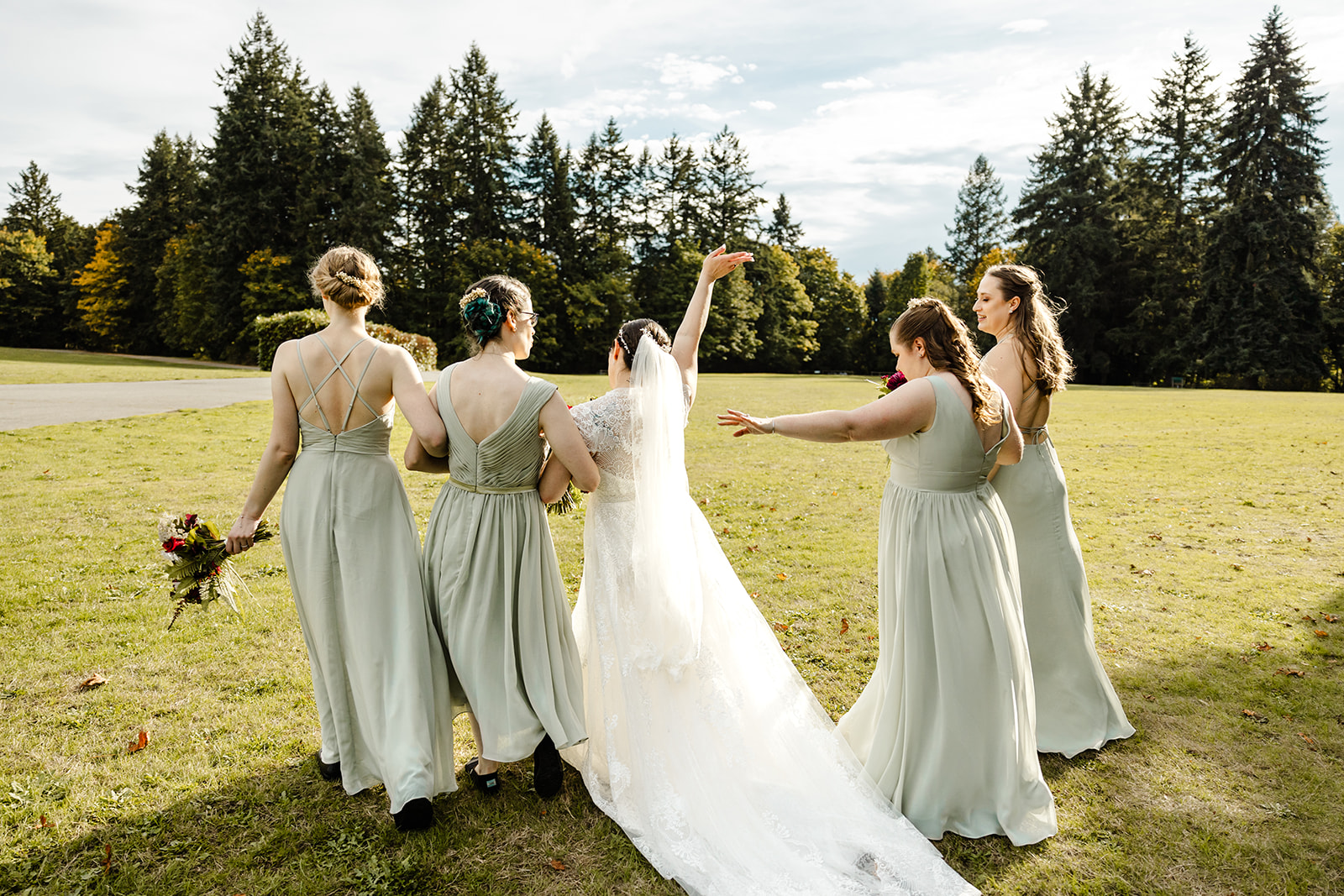 bride waves her arm in the air as she walks across lawn with her bridemsaids