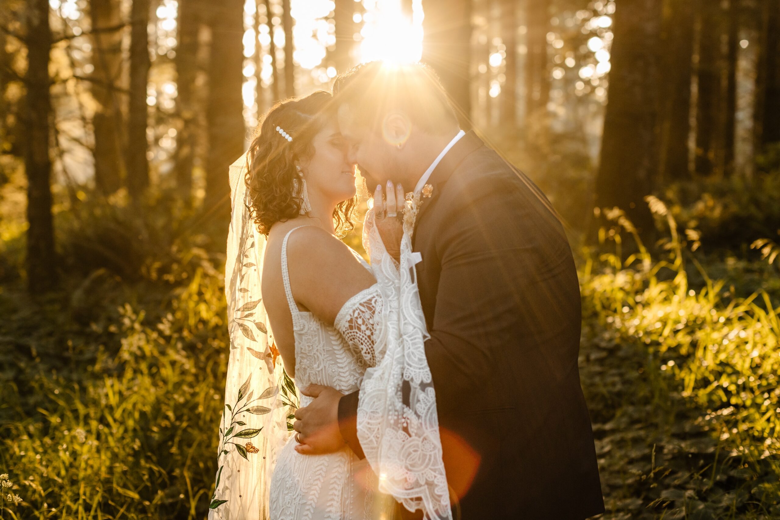 golden glow behind newlywed couple kissing with dramatic lace sleeves on wedding gown