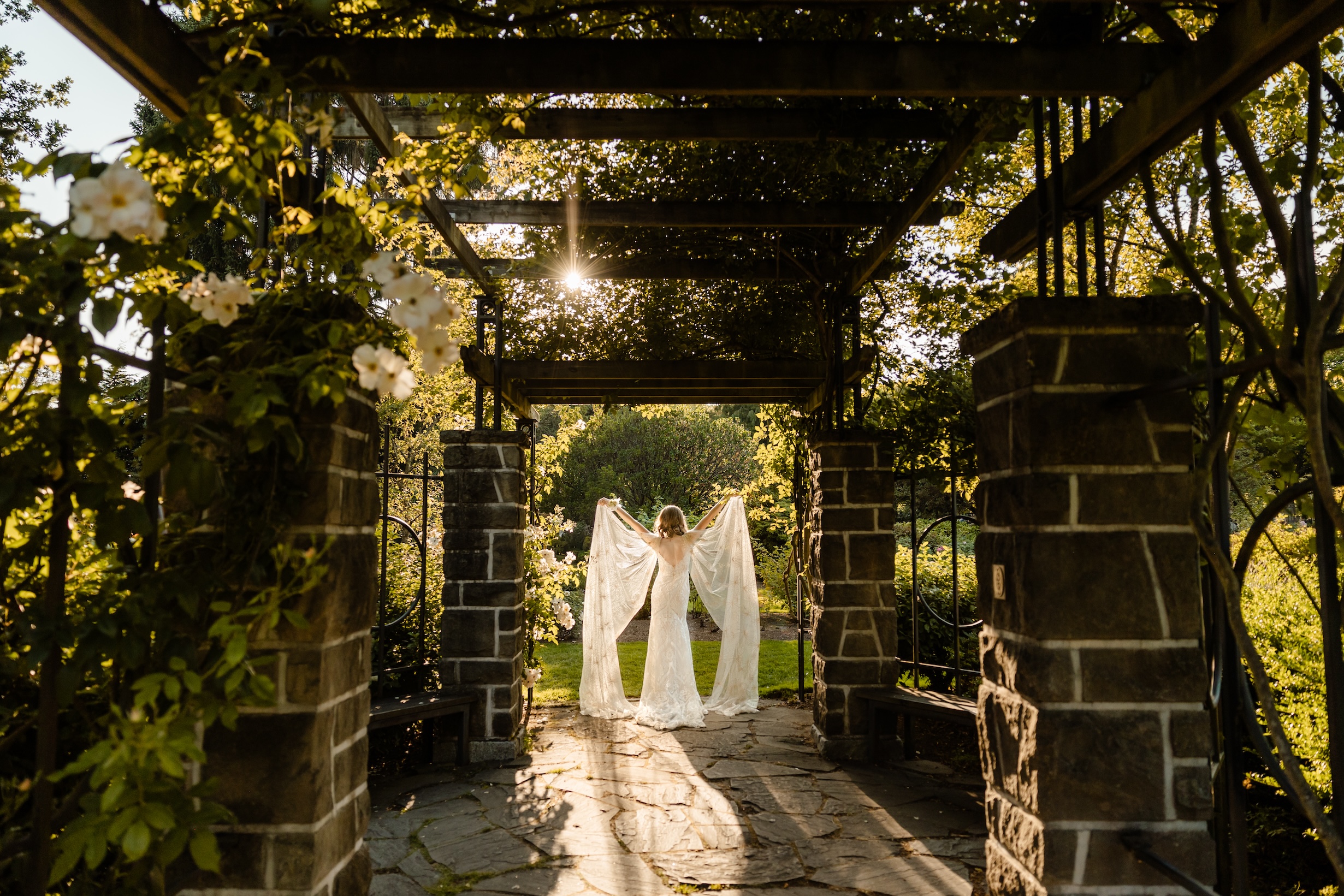 bride holding up cape in sunlight at woodland park rose garden 