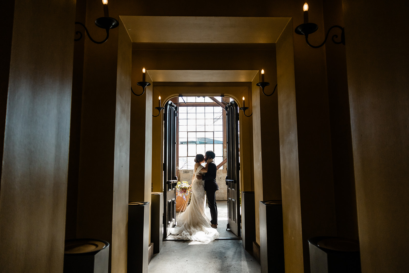 bride and groom stand at the end of a long hallway in a door