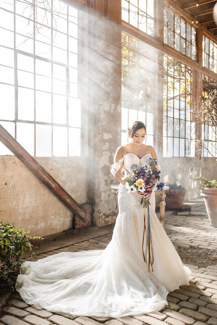 bride stands in front of windows holding bouquet