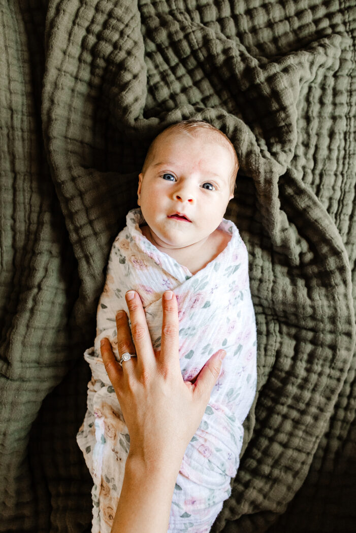baby lays on green blanket with hand on her