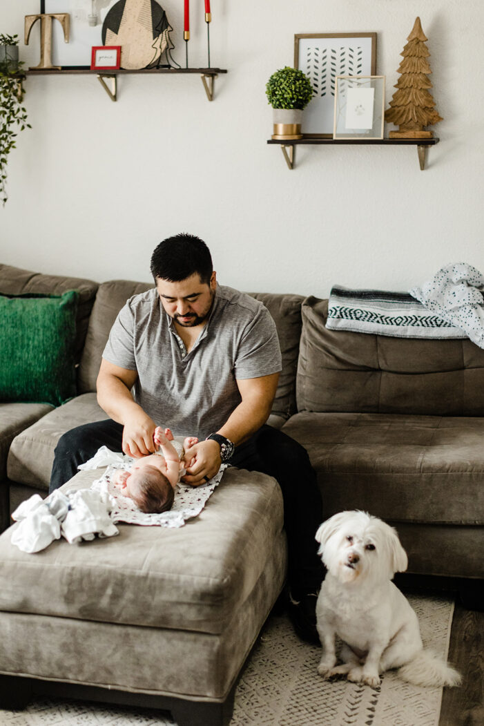 dad changes baby while dog looks on