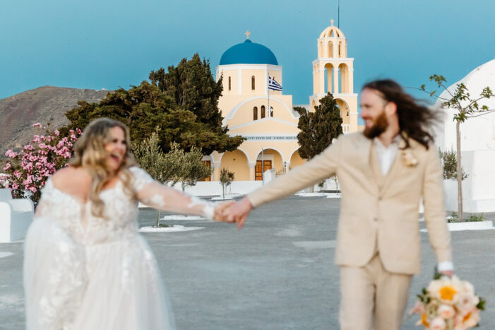 bride and groom hold hands as they walk through santorini