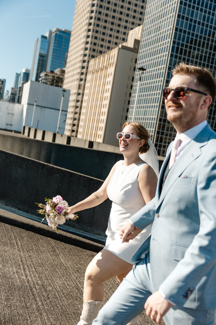 bride and groom walk in front of seattle skyline