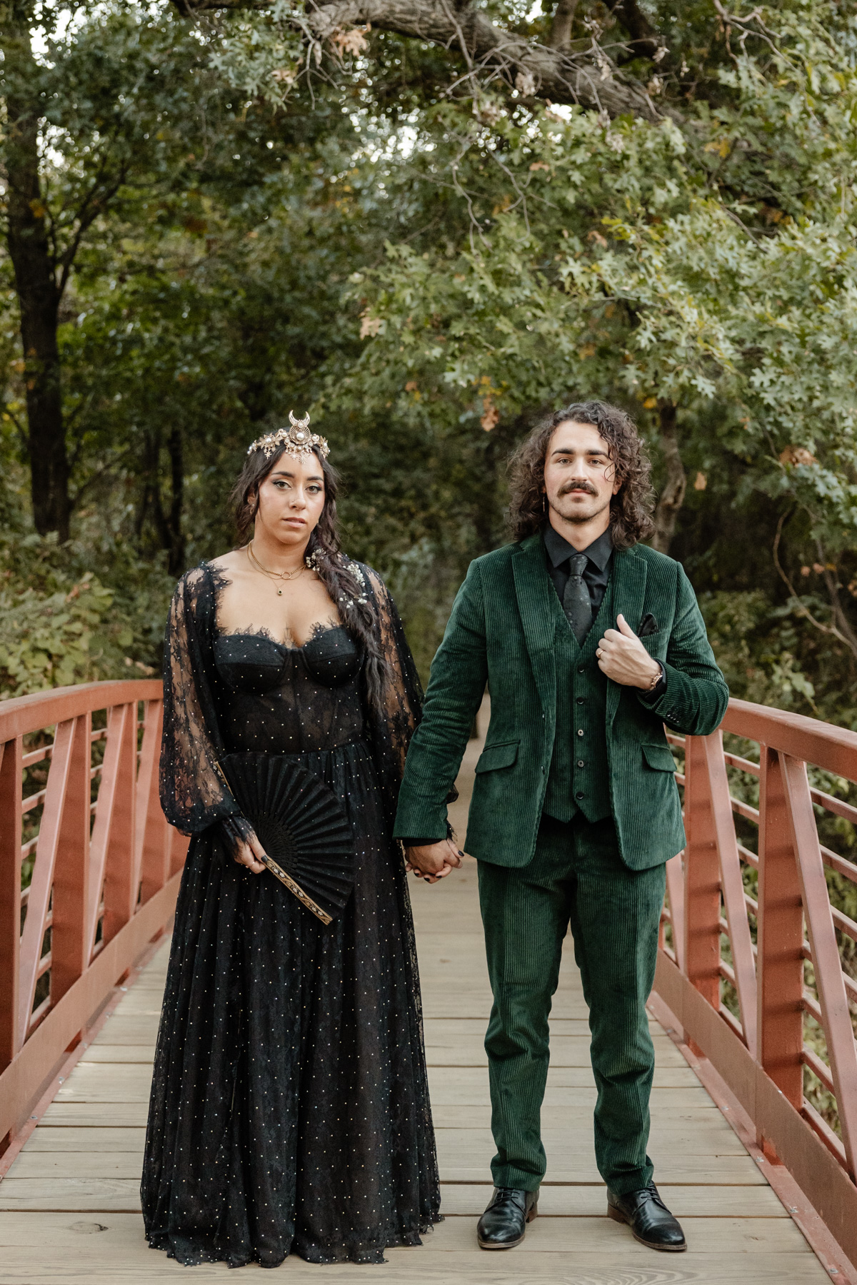 bride wearing crown and black lace wedding dress, groom in velvet emerald green suit