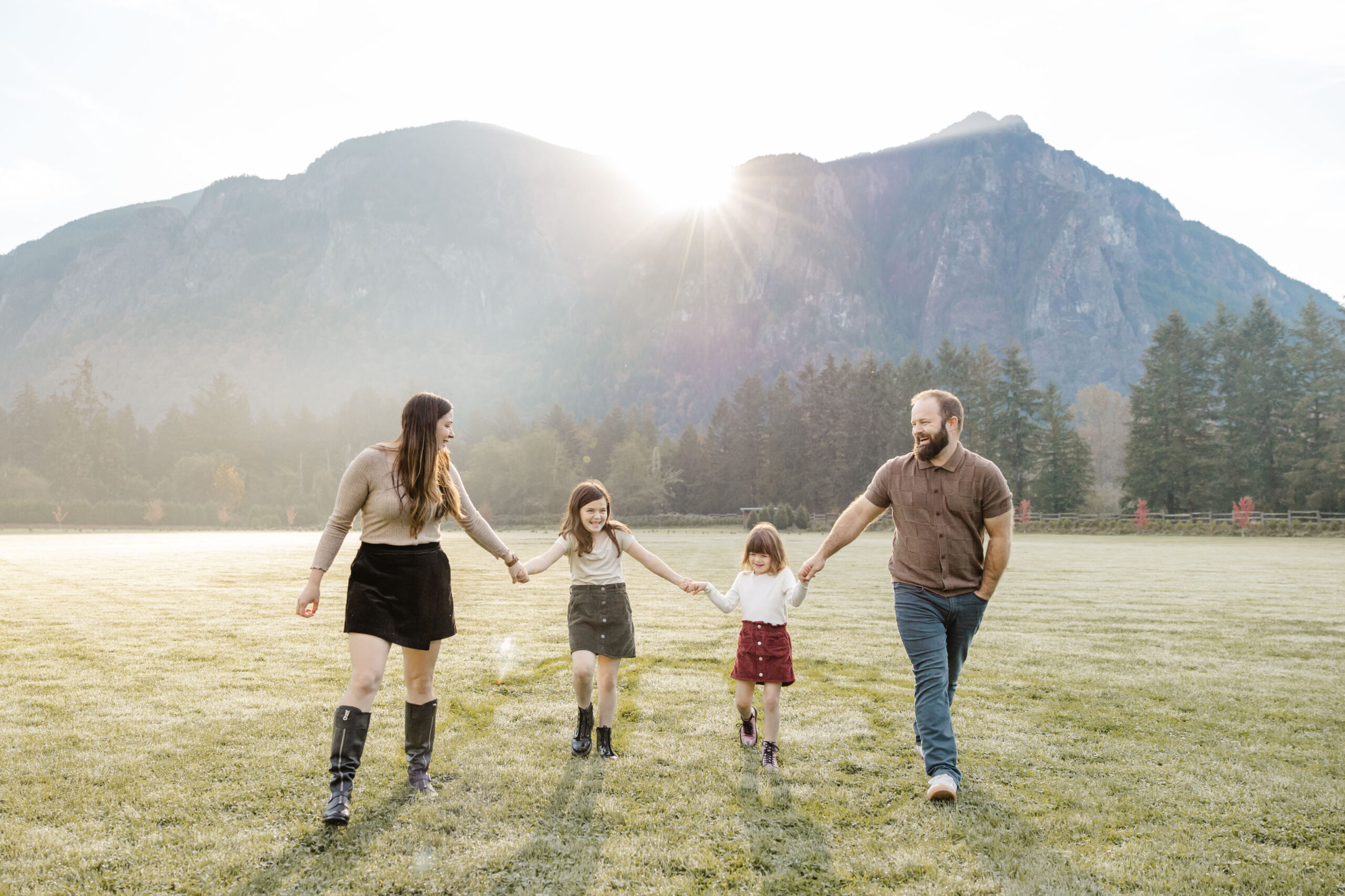family holding hands walking towards camera with sunshine peeking over a mountain