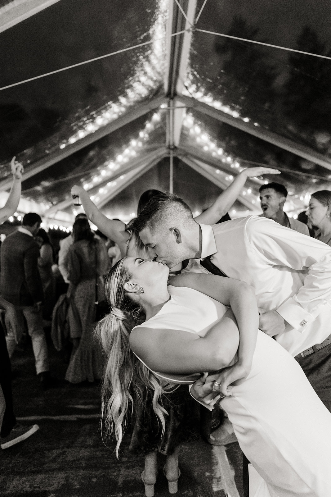 wedding rain plan under a clear tent with twinkle lights bride and groom kiss