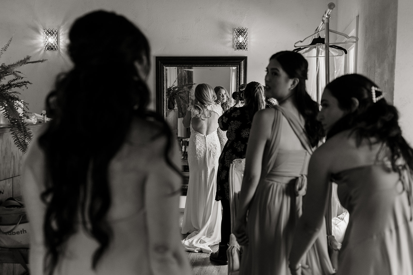 bride looks in mirror while bridesmaids look on