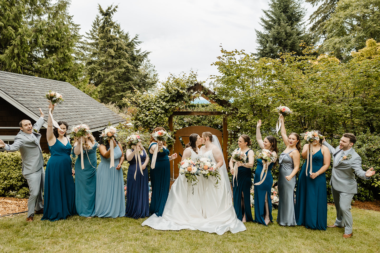 brides kiss with their bridal party in blue around them