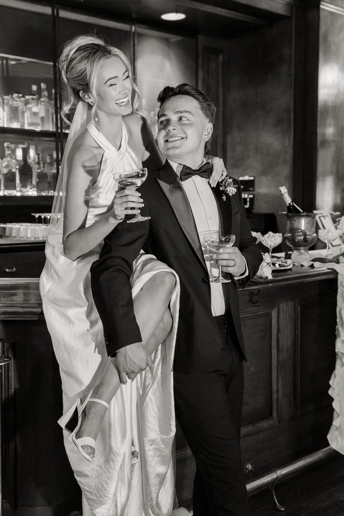 bride and groom smile while sitting atop bar