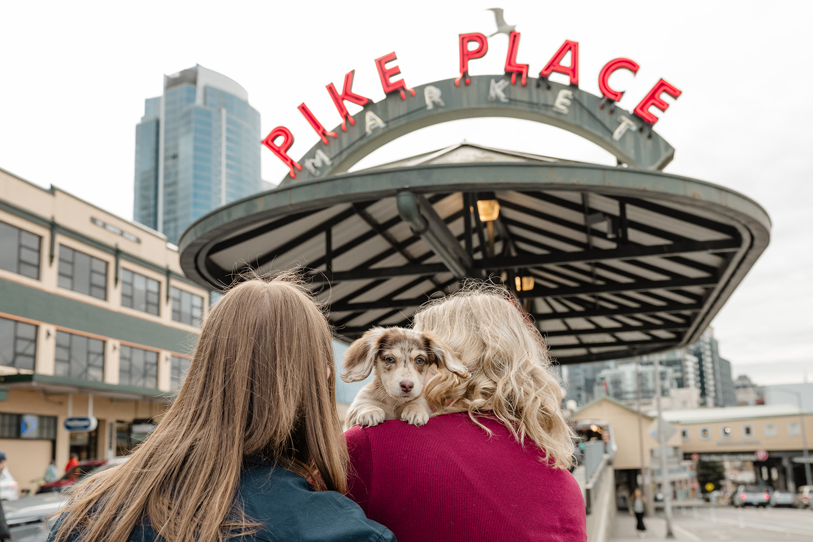 couple looks up at pike place sign holding small dog on shoulder