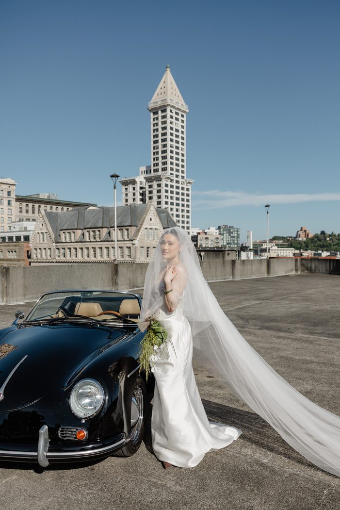 bride stands next to car with smith tower in the back