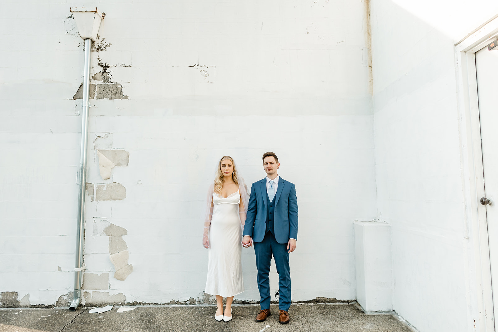 bride and groom stand beside each other in front of white wall