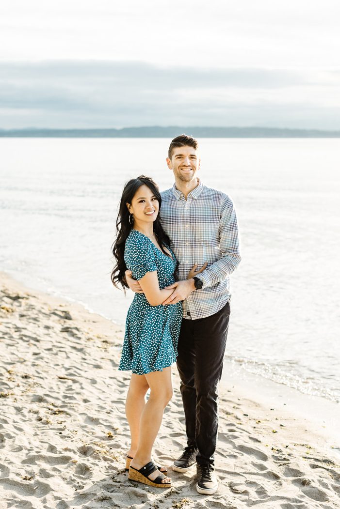 man and woman smile with ocean behind them